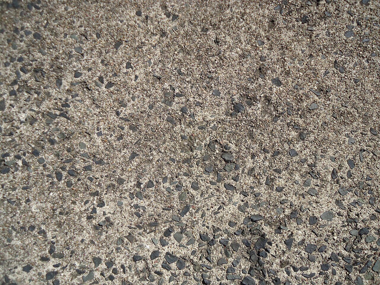 Close-up of a weathered exposed aggregate concrete sidewalk surface