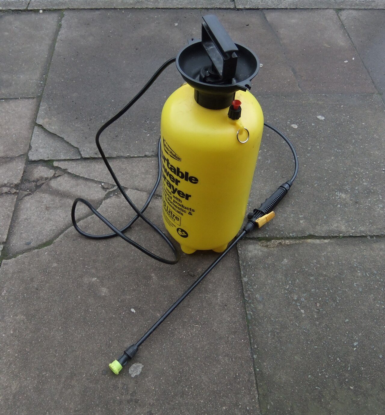 Yellow pump sprayer for cleaning solution resting on cracked stone paving