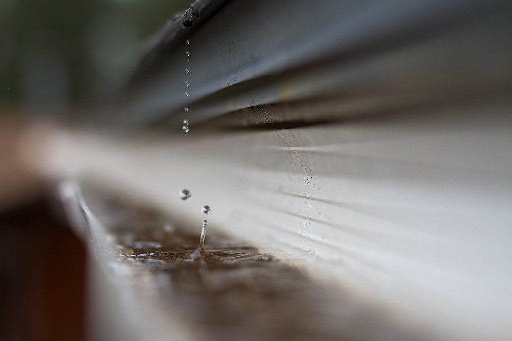 Rainwater dripping into standing water inside a metal gutter